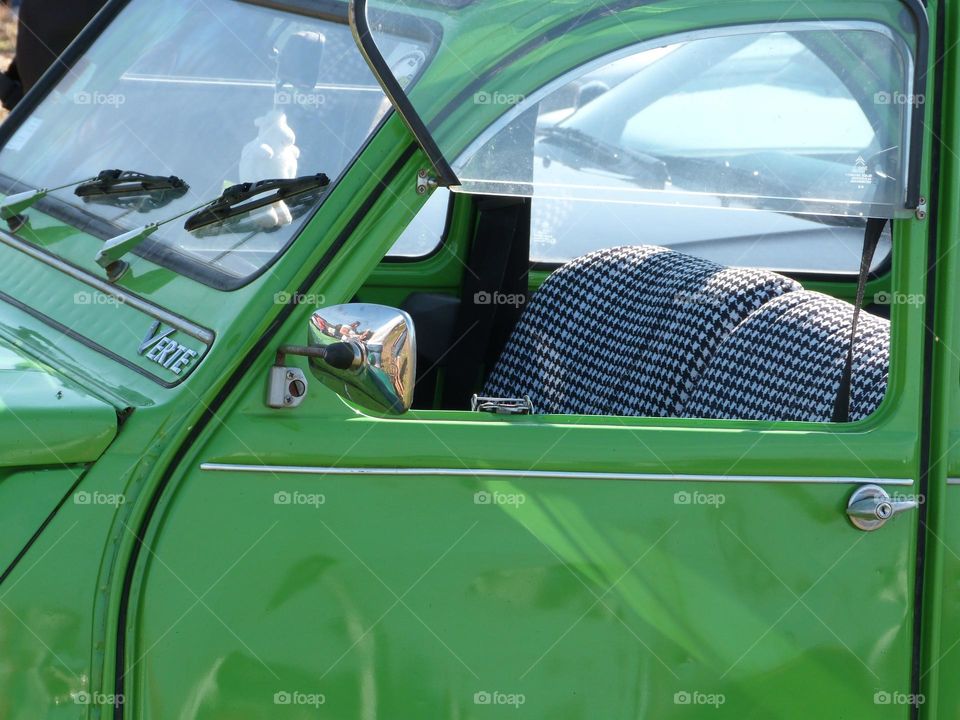 Une vieille voiture mythique, la Peugeot 2CV "verte" avec des sièges à motif Vichy noir et blanc.
A mythical old car, the "green" Peugeot 2CV with black and white Vichy seats.