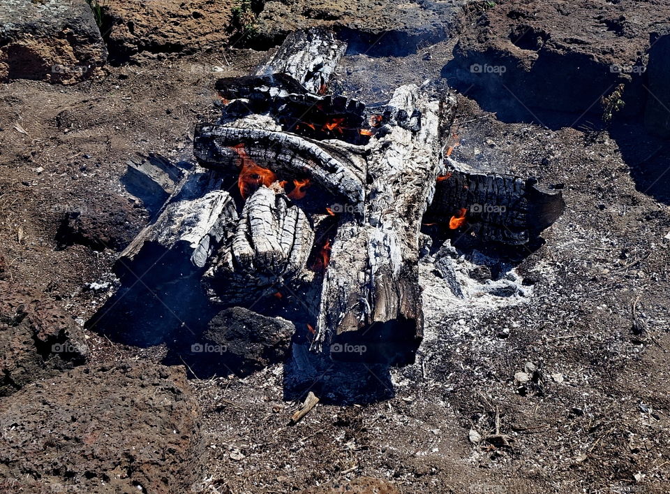 A huge fire pit burns down to coals and is ready to cook on. 