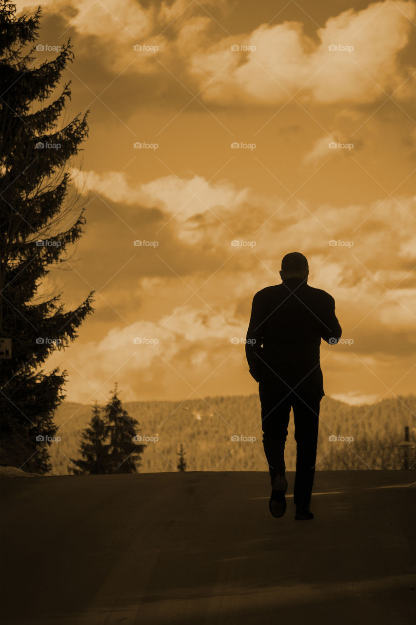 Silhouette of man walking uphill on a path through the forest