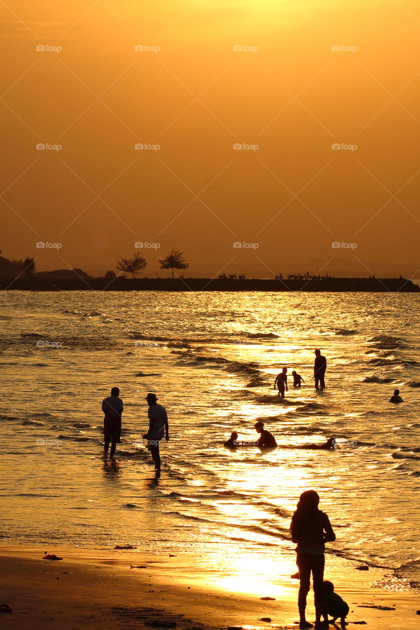 Some people playing at the beach, enjoying the sunset.