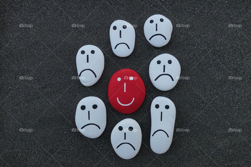 One happy person among many sad persons, conceptual composition with stone faces over black volcanic sand