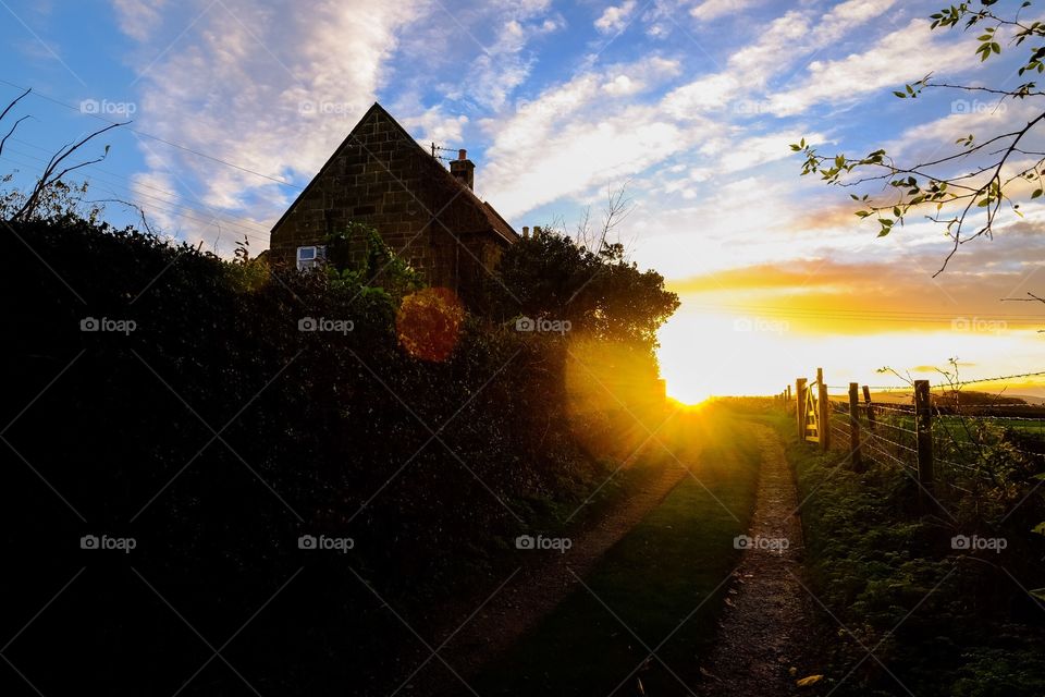 Sun up around the bend: the sun comes up at the apex of a bend in a farm track, with the farm house silhouetted against the sky. 