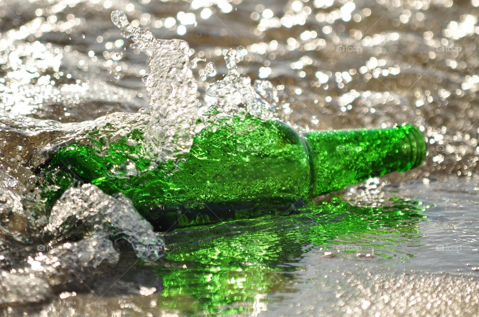 splashing water on the beach with green bottle