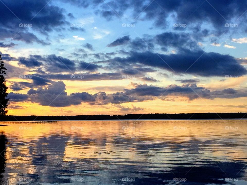 Stunning magic dramatic sunset over the smooth sea water surface with the multiple clouds layers reflection 