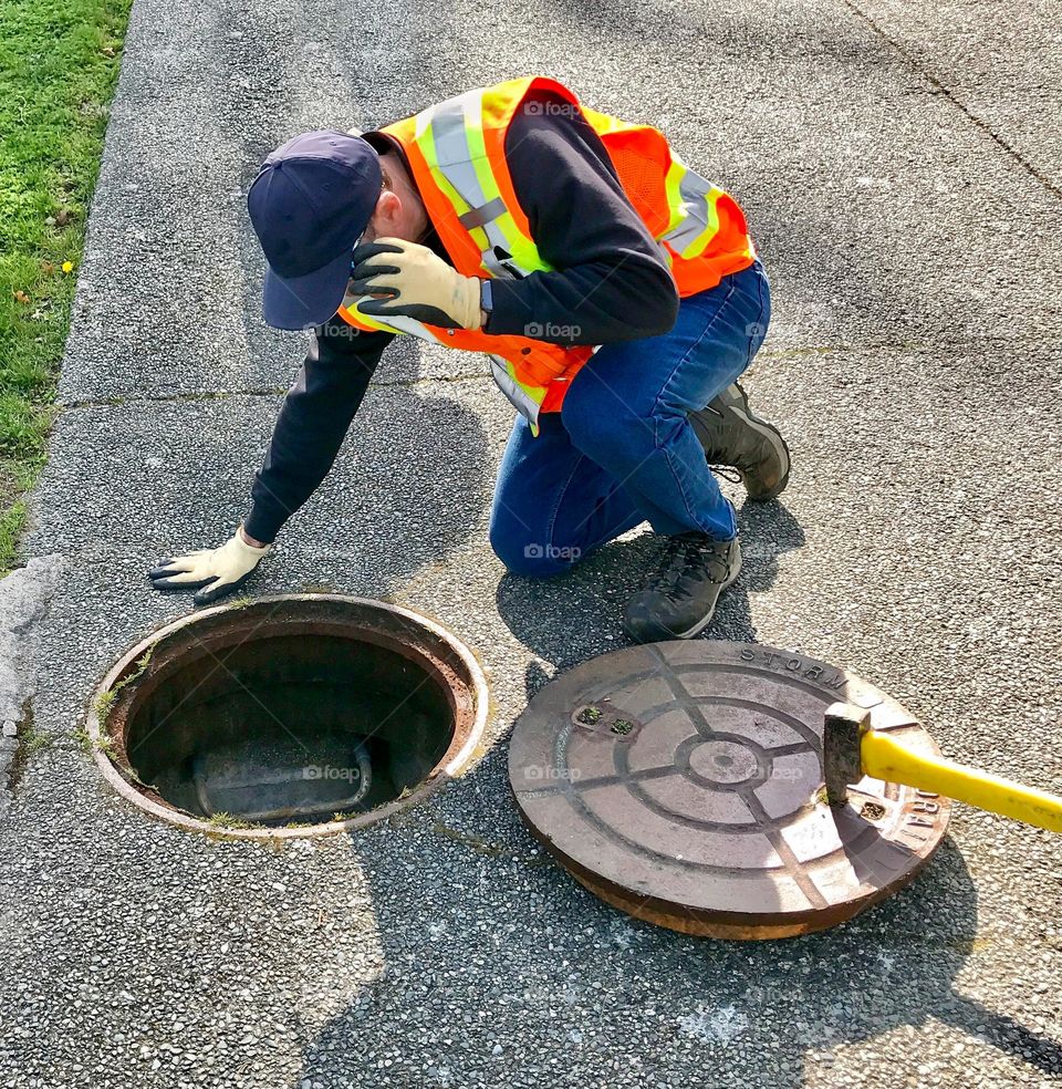Town worker looks down a manhole to check for blockage 