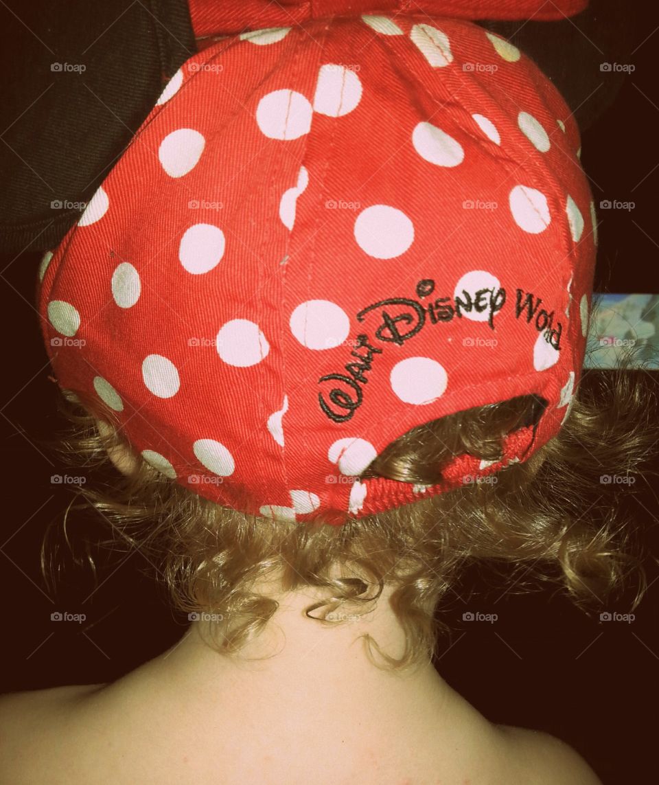 toddler girl wearing a disney world minnie mouse hat with her baby curls sticking out