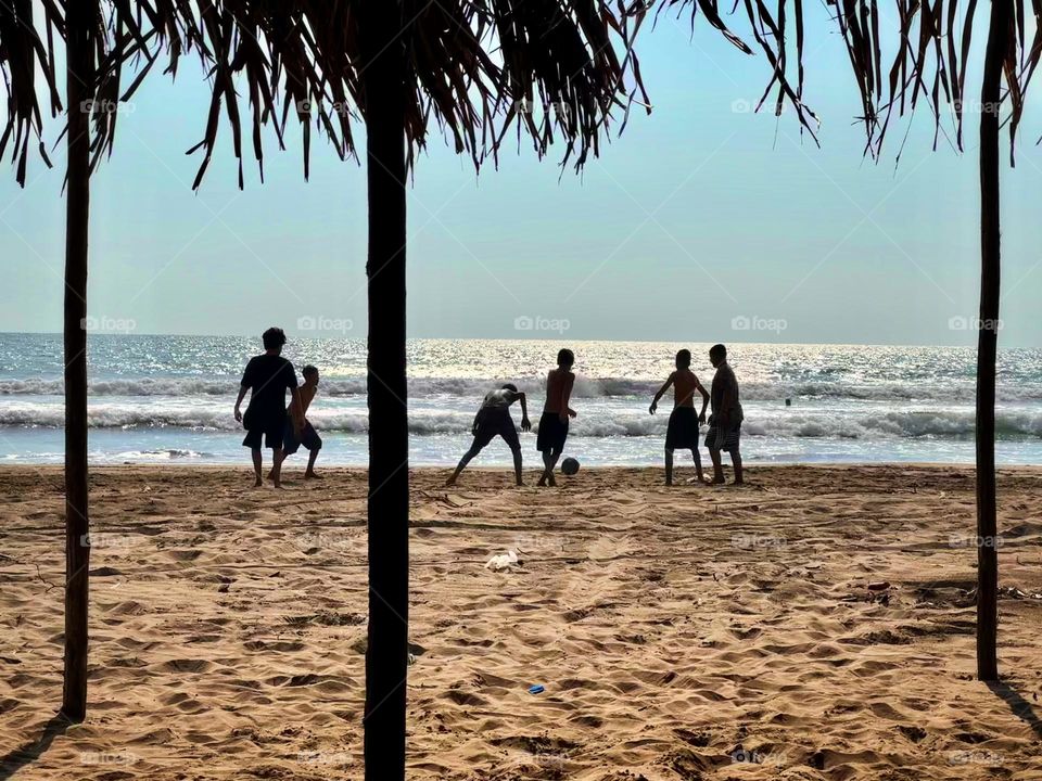 Group of little men playing football soccer in the beach, in a sunny day.