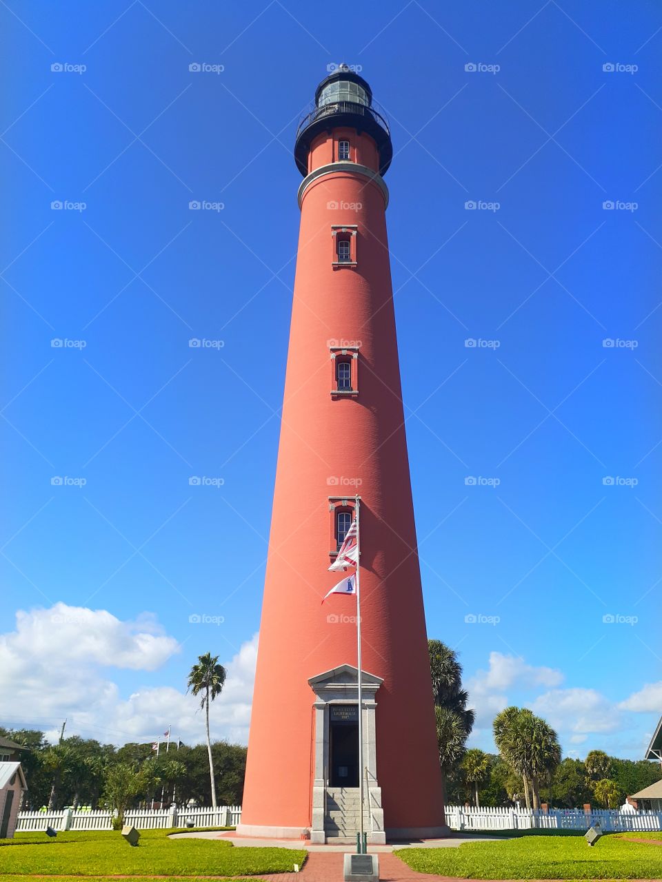 The red Ponce Inlet Lighthouse in Ponce Inlet, Florida. It is very tall with a flag in front of it.