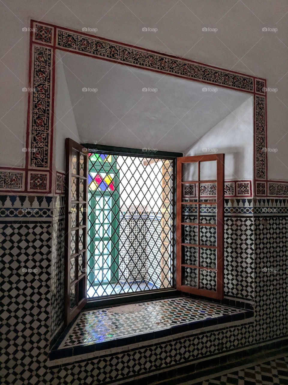 Colorful Diamond Pattern Stained Glass Window and Grate Surrounded by a Ceramic Tile Mosaic Wall in the Bahia Palace in Marrakech in Morocco