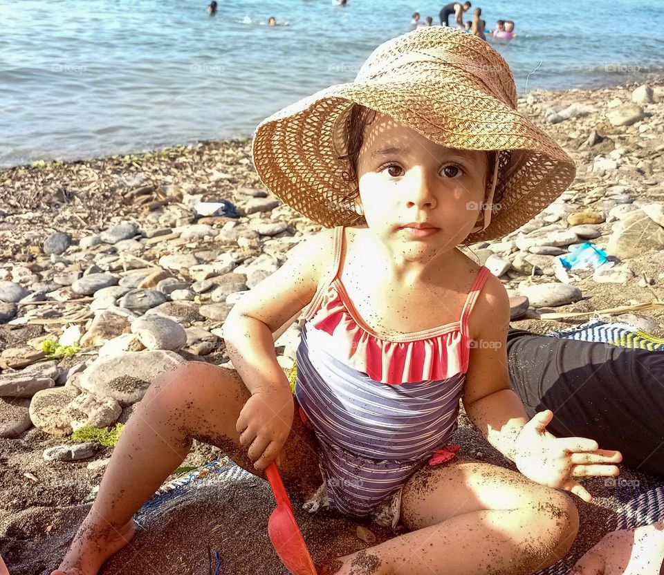 a young child on the beach wearing a hat and looking in the camera