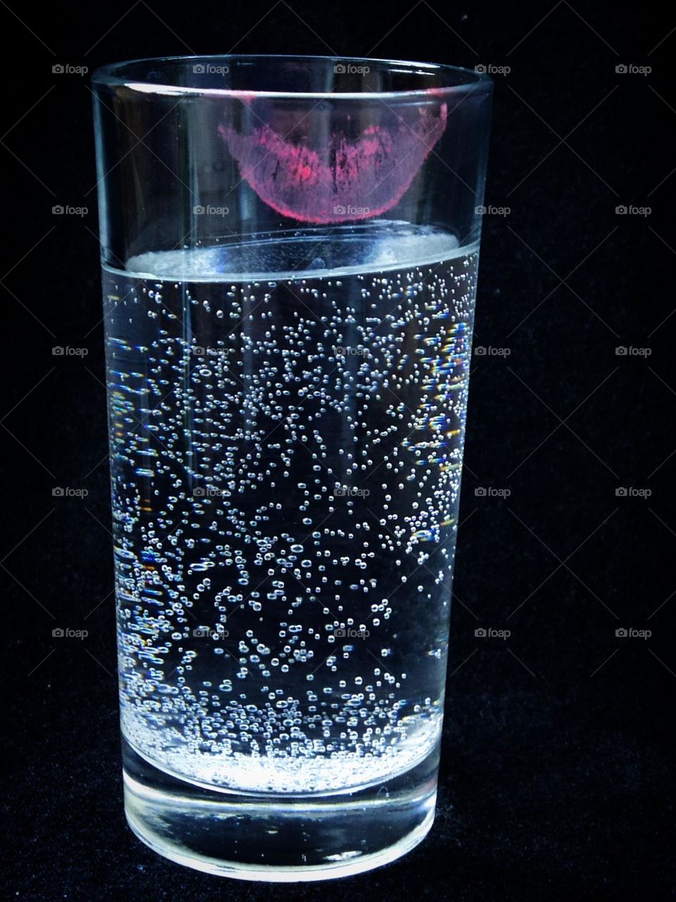 Minimalism.  Transparent glass with sparkling water.  There is a trace of lips from pink lipstick on the glass.  Black background