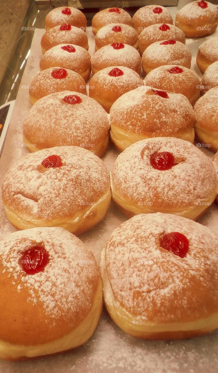 Many delicious big donuts with red fruit gem and sugar powder on in bakery arranged symmetrically on tray