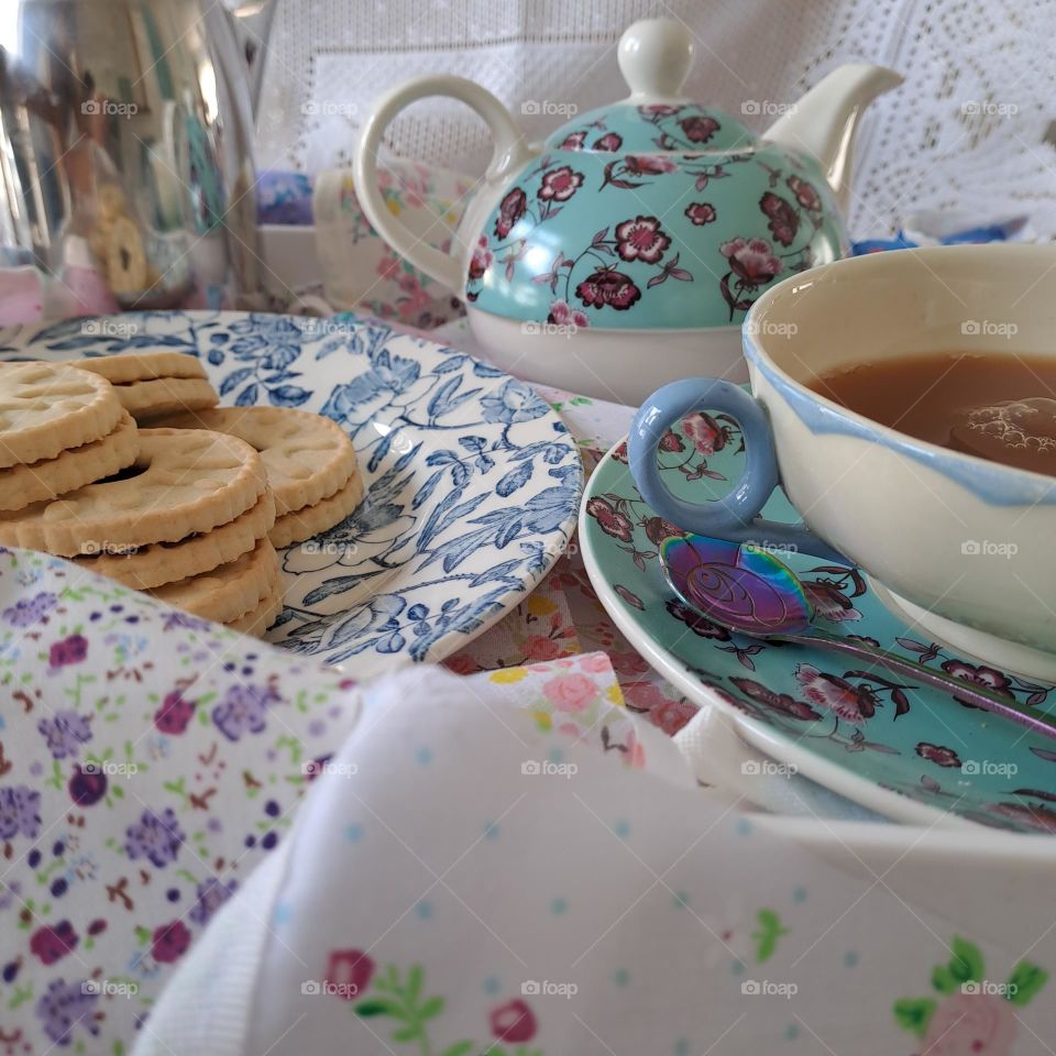 display of teapot and cup of tea very english in a cup with saucer with biscuits on a plate. bunting decorating the table