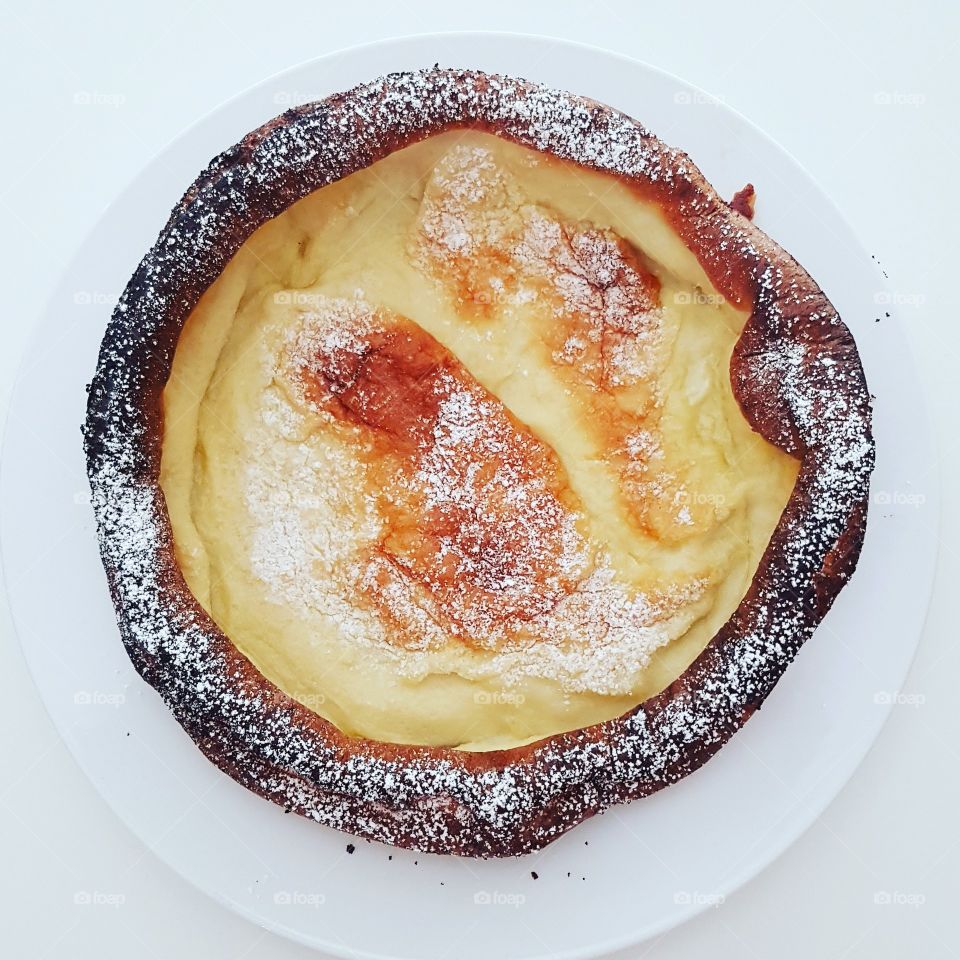 dutch baby oven baked pancake on a white plate and sprinkled with confectioner's sugar