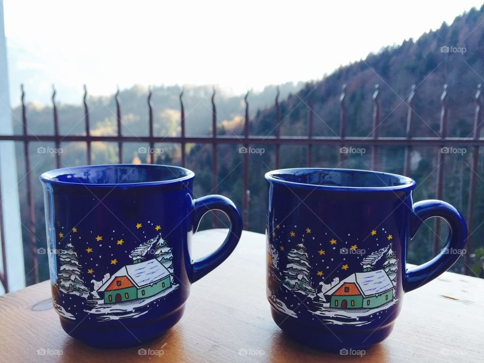 Two Christmas cups on the table with view of forest in the background