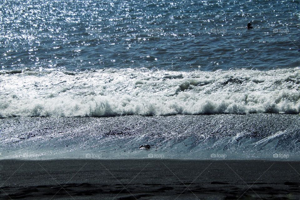 View of the blue Atlantic Ocean with waves, black sand beach and a swimmer