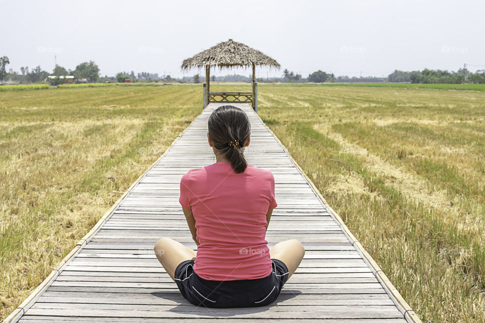 Woman sitting on a wooden bridge with a bamboo hut in the rice fields.