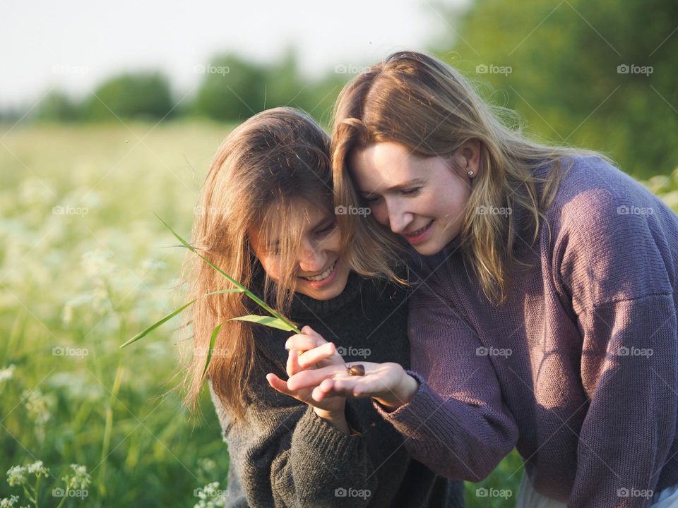 Two happy girlfriends in the blooming field on the sunny summer day