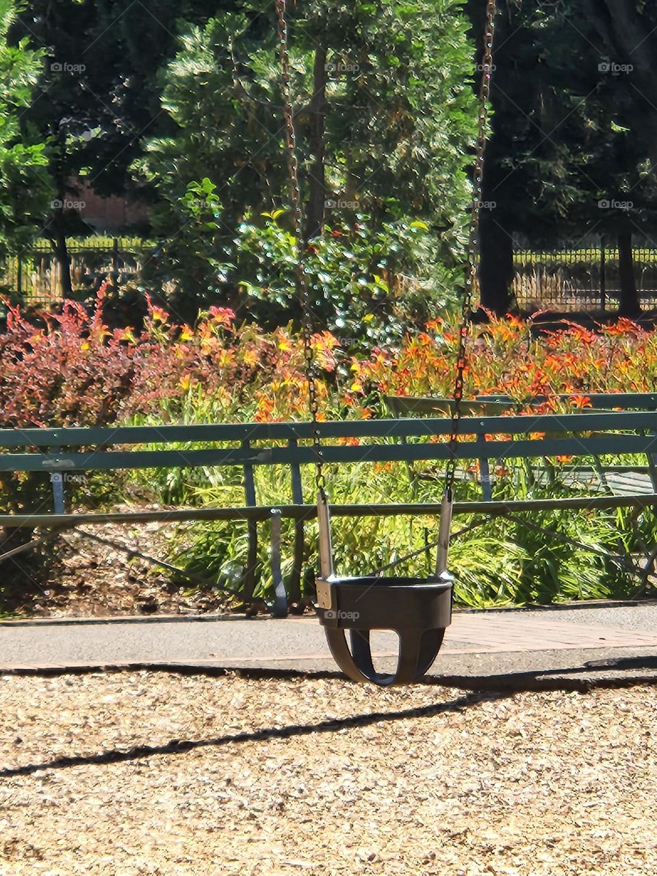 single black swing for children in an Oregon park in Summer with brightly colored benches and flowers in the background