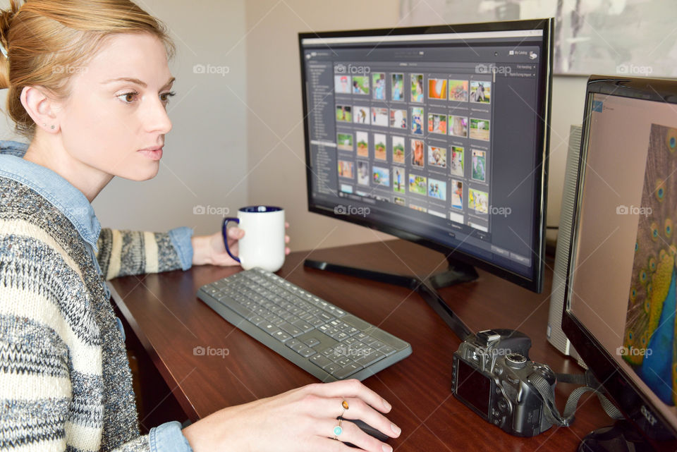 Woman sitting at a desk with a digital camera and editing pictures on a computer monitor