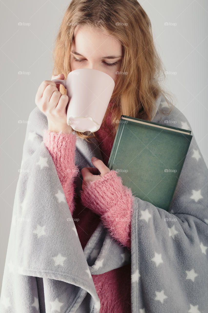 Enjoying the drinking coffee and reading a book. Young girl holding book and cup of coffee going to relax at home