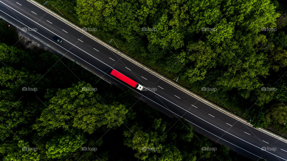 Red car on the highway, that leads through the green forest 