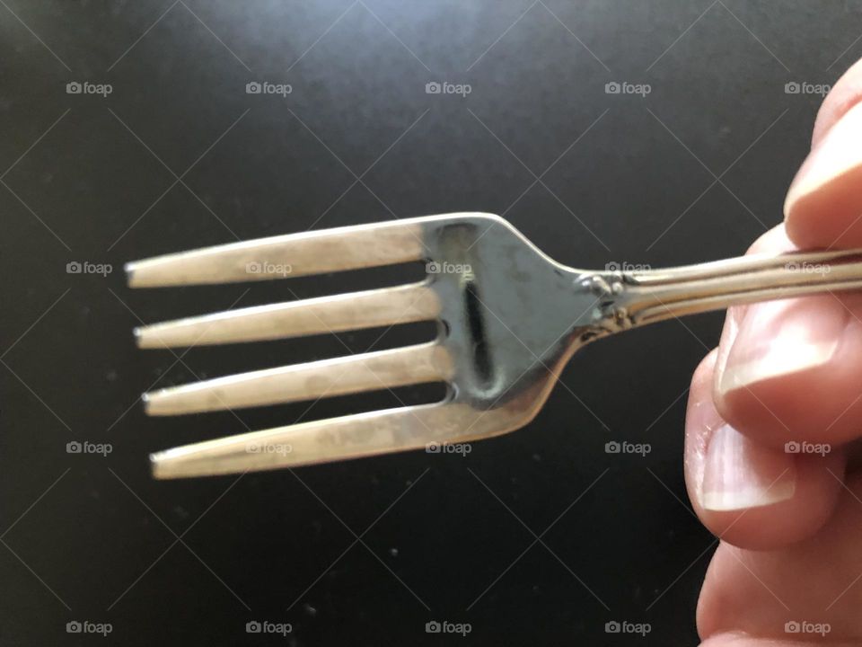 Closeup of hand holding small fork only fingers visible lens reflection looks like a mouth in surprised expression 