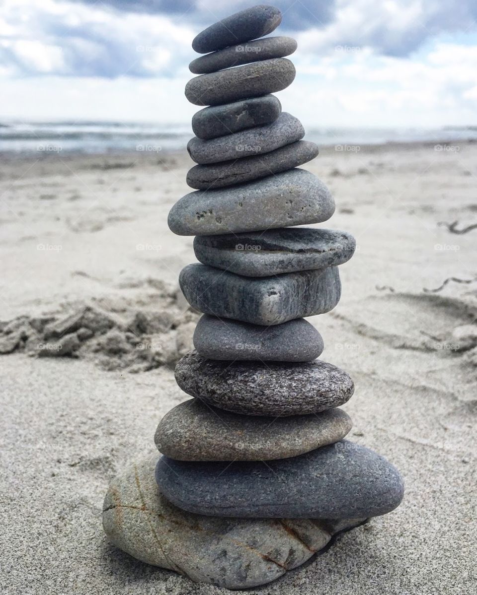 Cairn tower of gray beach stones and rocks on sandy beach. 