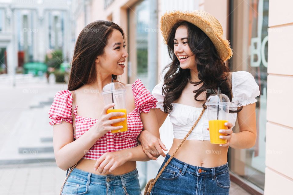 Happy smiling beautiful brunette young women friends in summer clothes walking at the summer city street