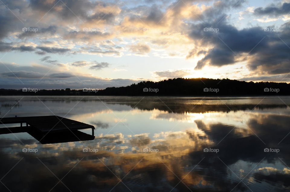 Silhouette of pier and clouds reflecting on lake during sunset