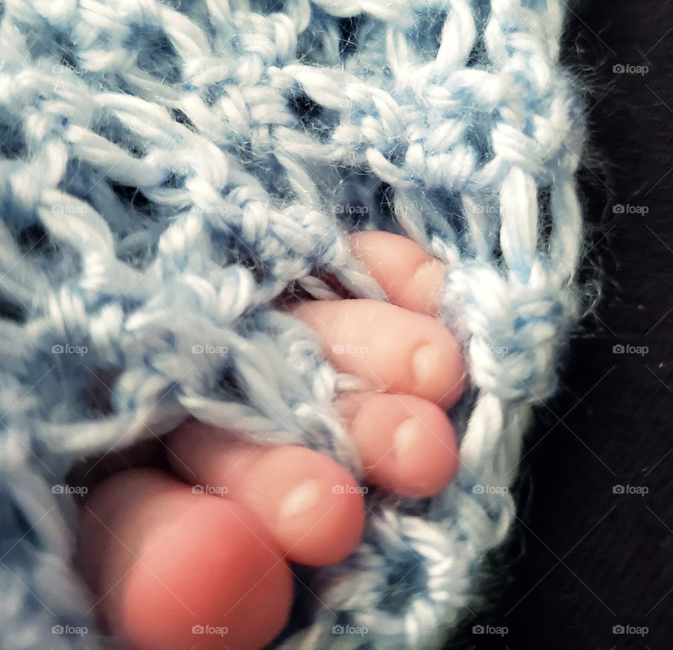 Beautiful tiny little toes poking through a baby blue knot blanket.