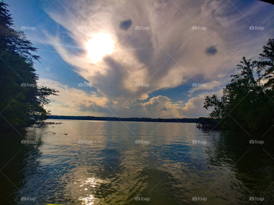Sun beginning to set over water in a lake cove. includes odd looking clouds, reflections and shimmering ripples.