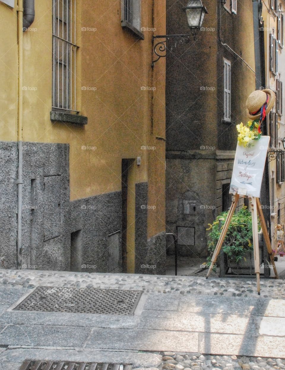 Sign with a hat. A cobblestone walkway in a small Italian village with a sign decorated with the hat and flowers