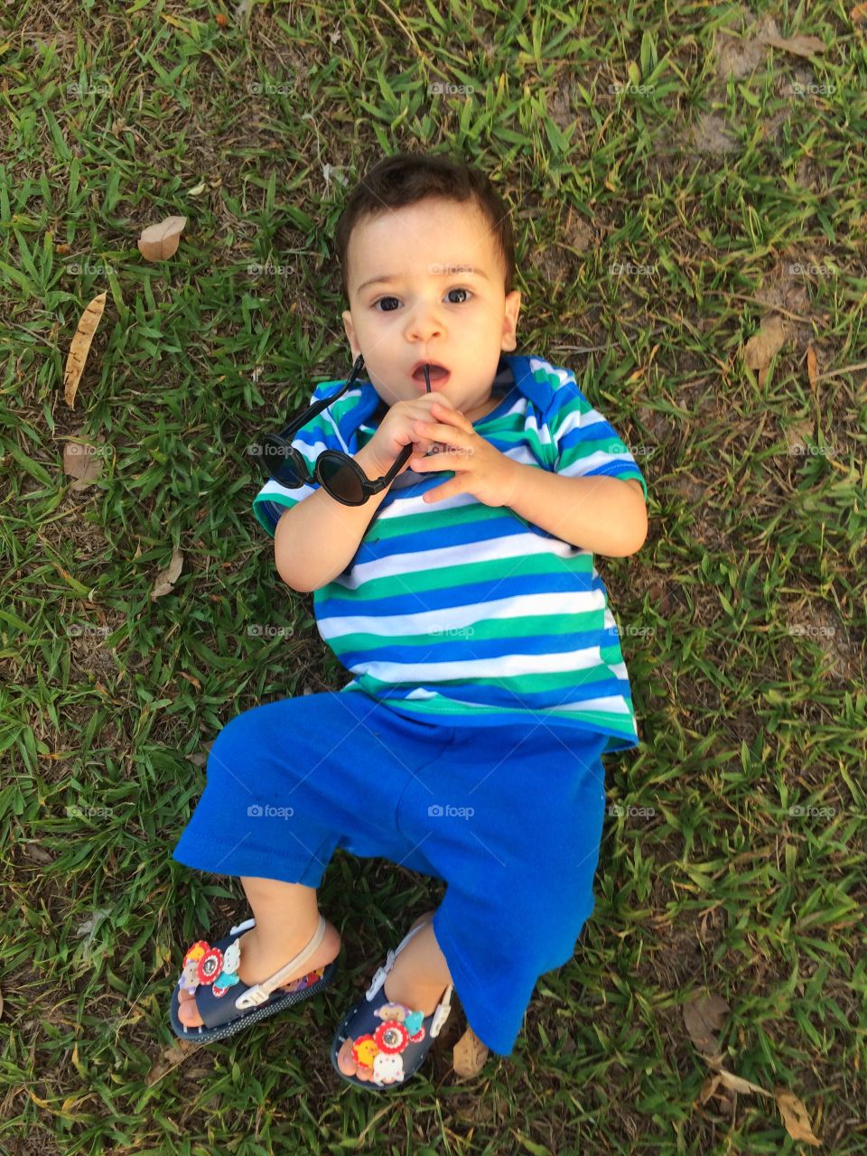 Elevated view of a cute boy lying on grass holding goggles