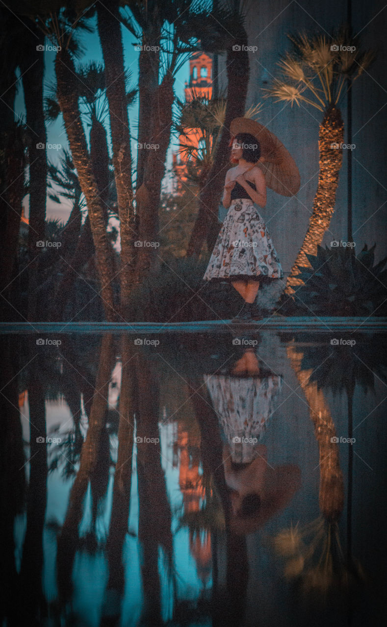 reflection of a woman holding an umbrella by a pond