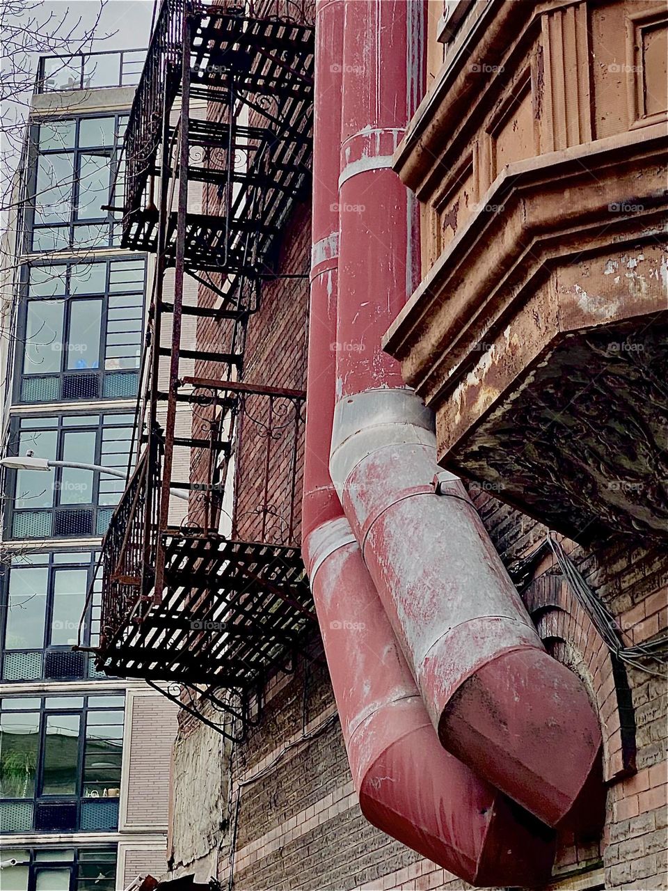 In “Clinton Hill”, Bklyn an old brownstone building on “Waverly St” off “Fulton St” always offers interesting photo opportunities like this from underneath view of the fire escape, parts of the facade and piping. 2023. Hypnotic Productions