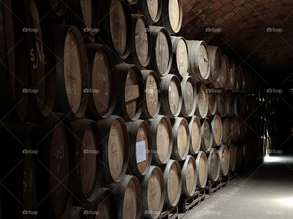 Group of brown barrels stacked in a dark corridor illuminated forming a curious pattern.
