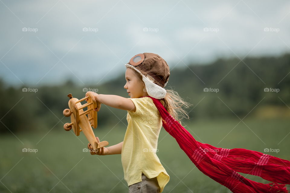 Little girl with wooden plane in the summer field 