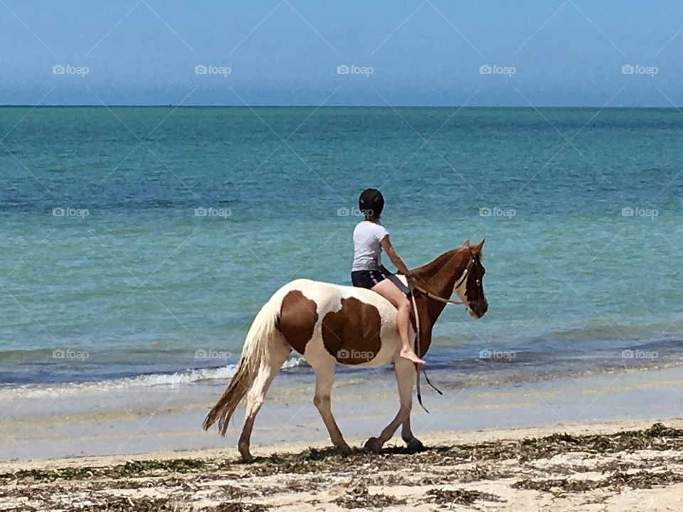 Barefoot rider 12 year old girl on horse riding along seashore