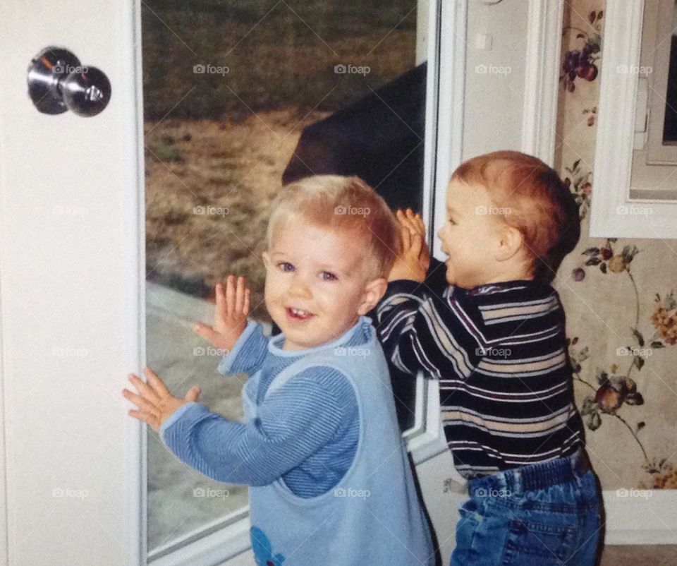 2 boys see something amusing outside while looking through window