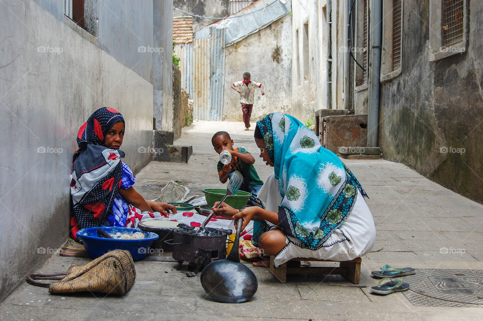 Two women with children cook food on the streets of Stonetown on Zanzibar.