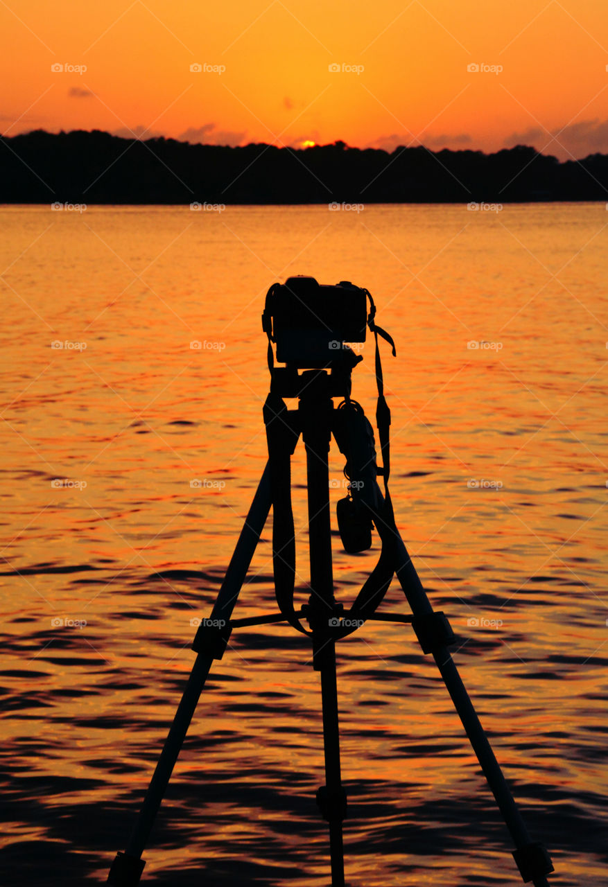 Silhouette of tripod and camera at beach during sunset