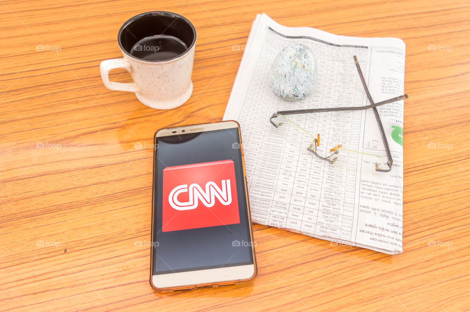 Kolkata, India, February 3, 2019: CNN news app (application) visible on mobile phone screen beautifully placed over a wooden table with a newspaper and a cup of coffee. A Technology Product Shoot.