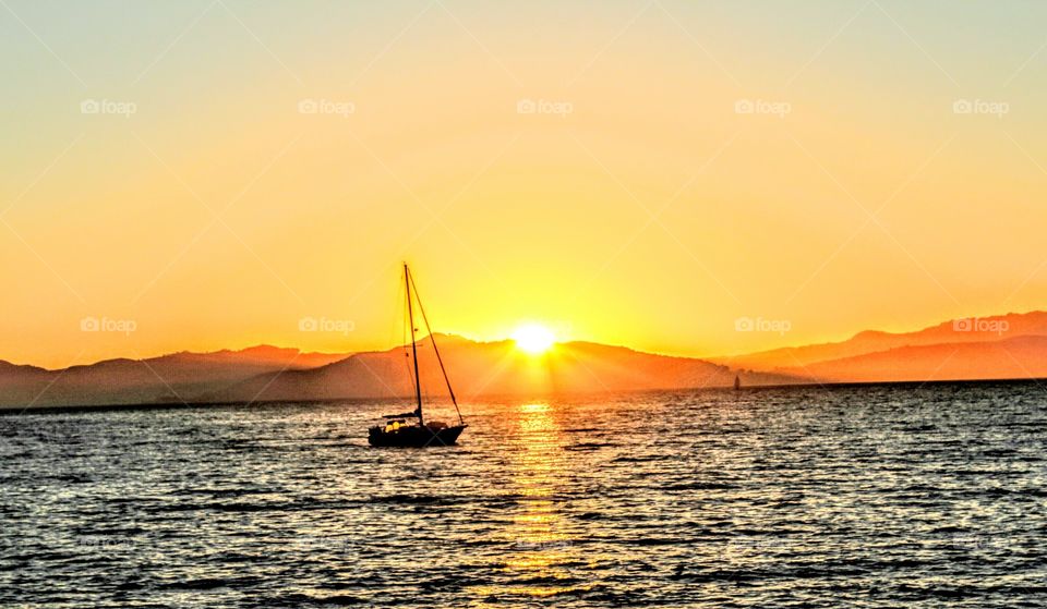 watching the sunset listening of the water while going down behind the mountains as a sailboat sails by