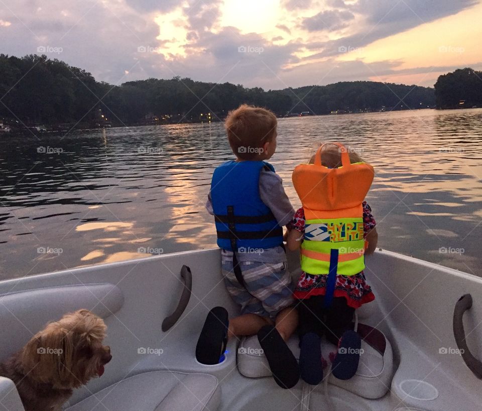 Evening boat ride after dinner illustrating the unique bond between siblings and their pet dog enjoying the warm summer breeze and the sunset reflecting on the lake 