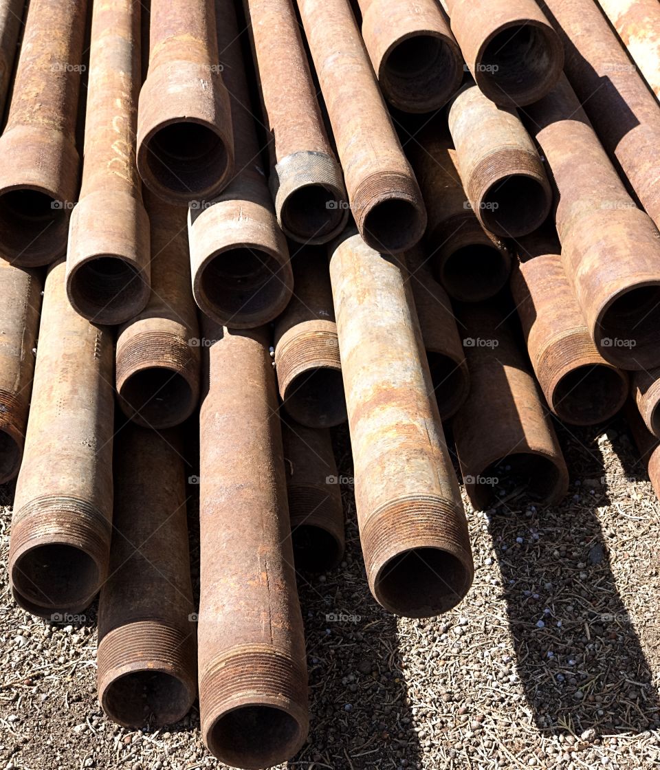 A close-up of rusted pipes with finely detailed threads stacked up on a site on a sunny spring day in Central Oregon. 
