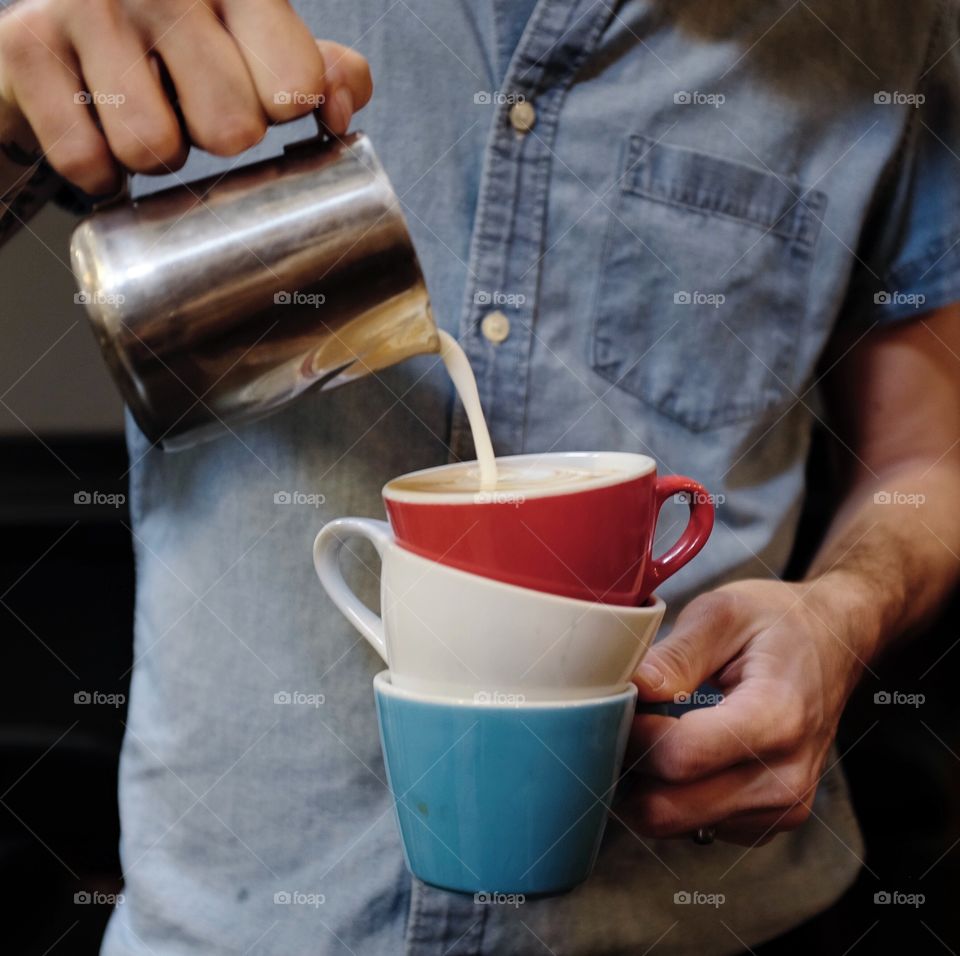Men pouring coffee on stack of coffee cups