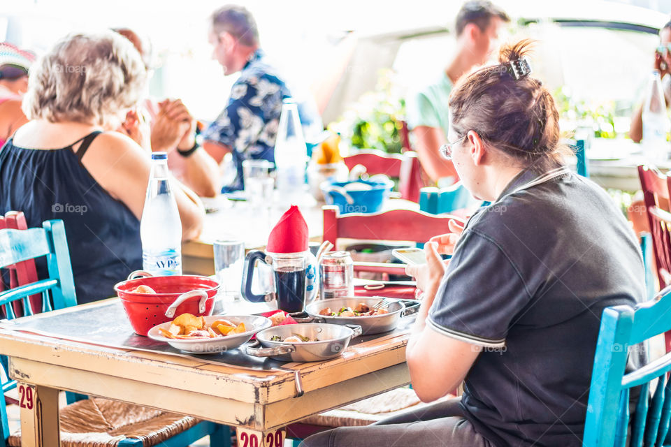 Young Woman Using Her Smartphone At An Outdoor Greek Tavern/Restaurant
