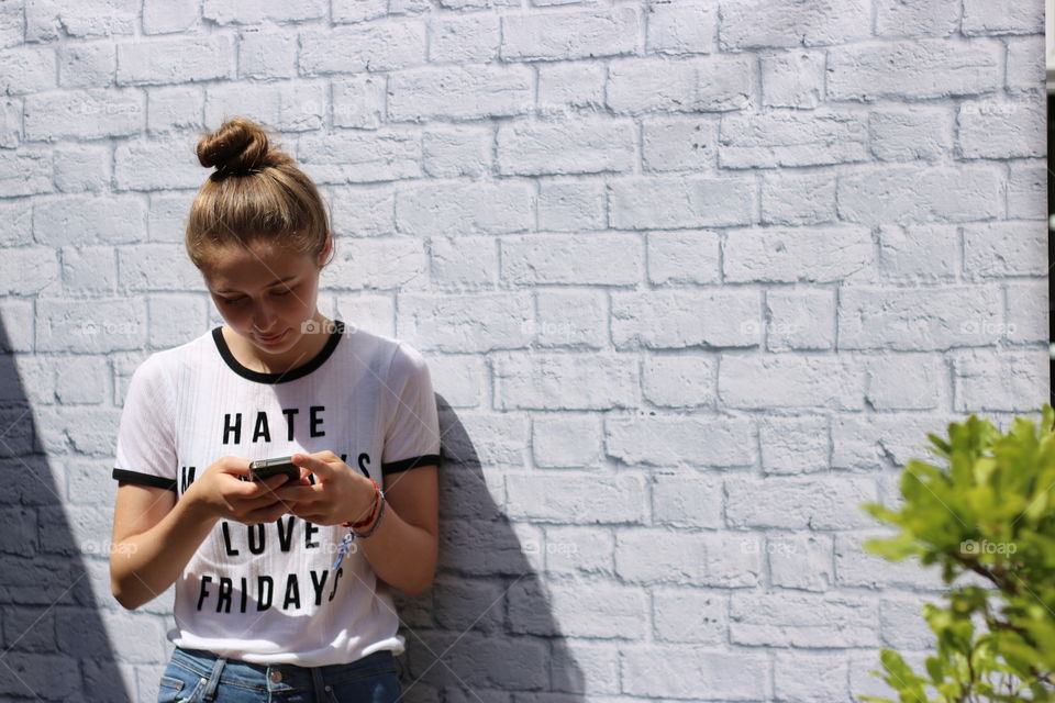 Young girl using mobile phone against wall