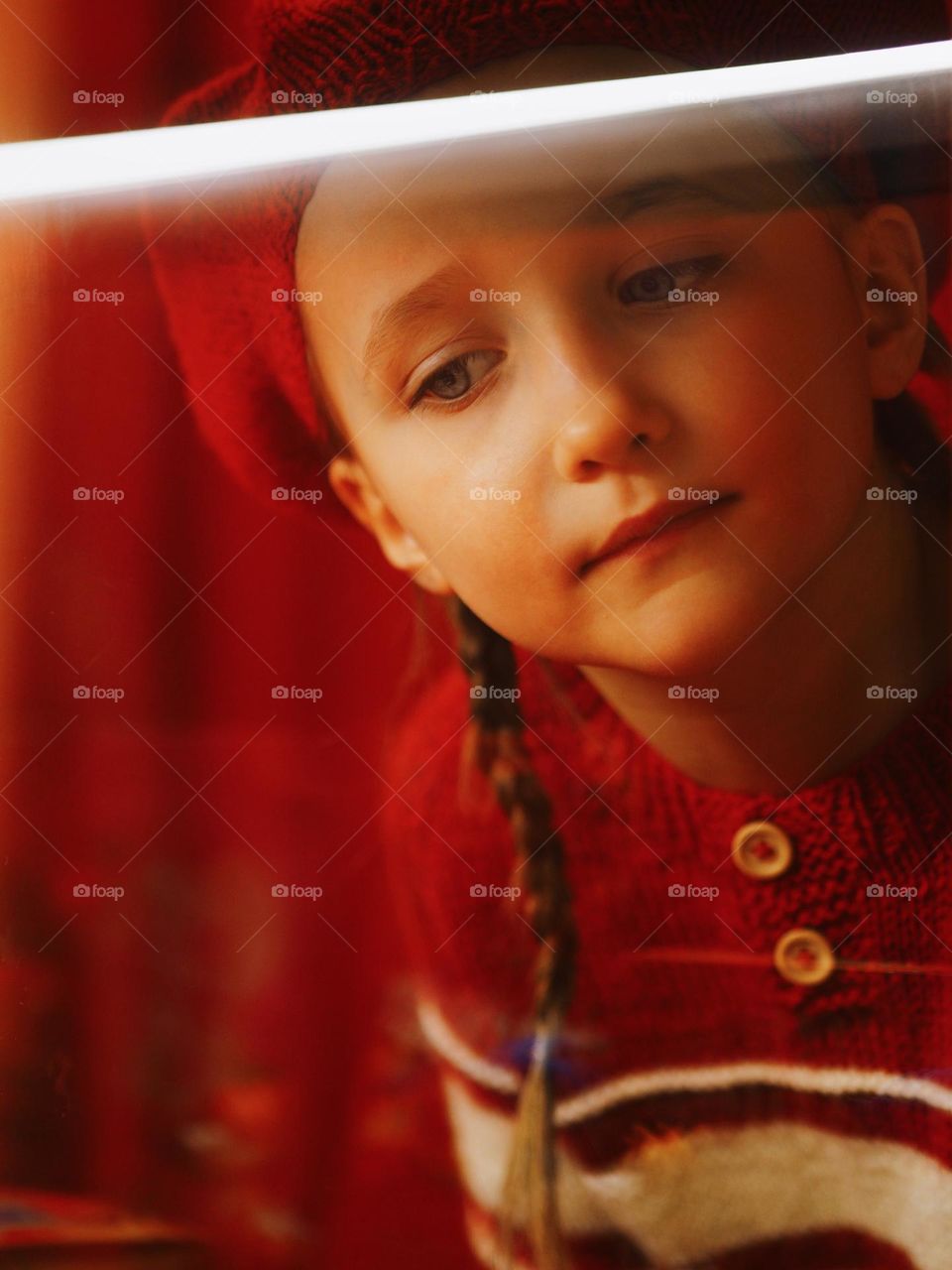 Portrait of cute little girl wearing red knitted sweater and beret looking at window, portrait of child 